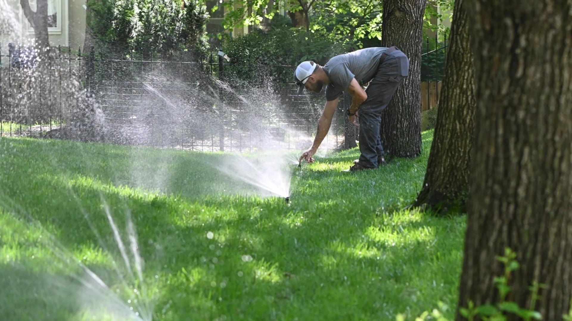 Technician adjusting lawn irrigation system in a residential yard.