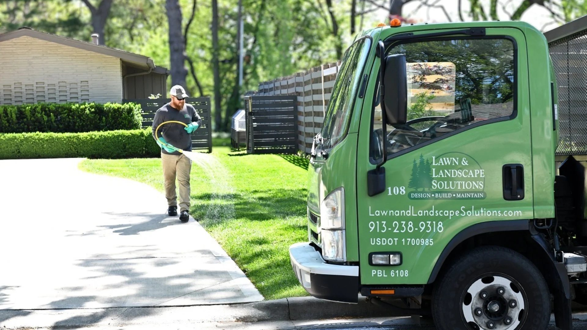 Lawn tech spraying fertilizer near truck.