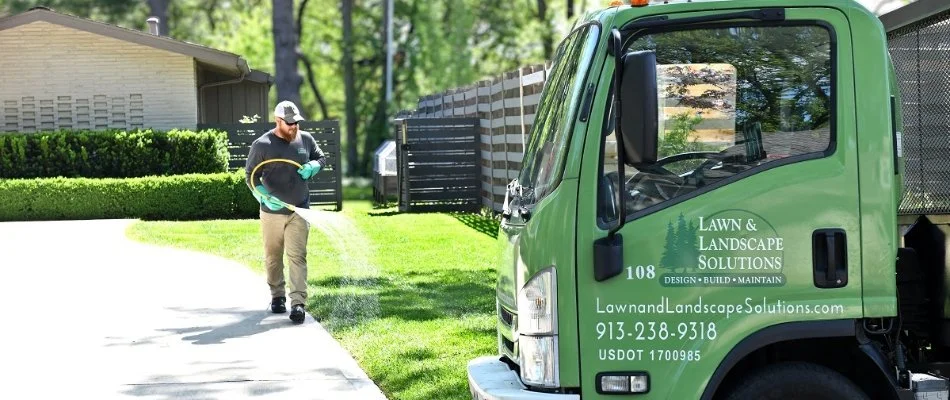 Man near a truck in Overland Park, KS, applying liquid fertilizer on a lawn.