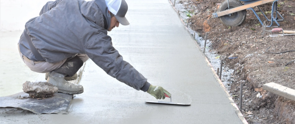 Professional landscaper smoothing concrete walkway by hand.